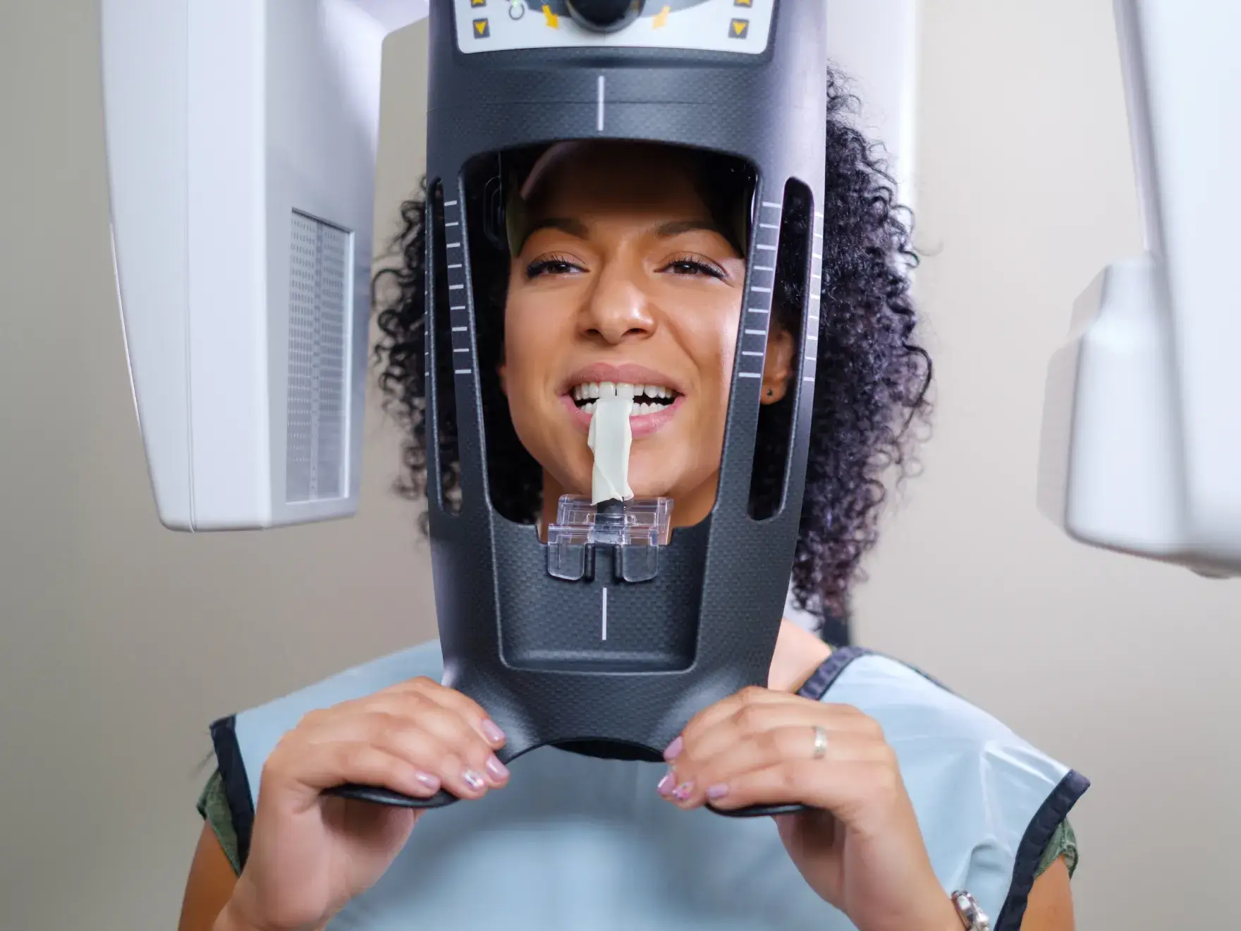 A person using a panoramic dental X-ray machine, biting a white piece for alignment.