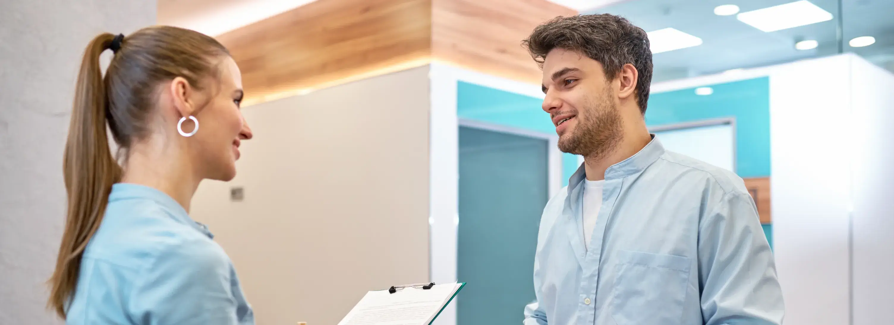 A photo of two people in light blue shirts talking in a bright office setting.