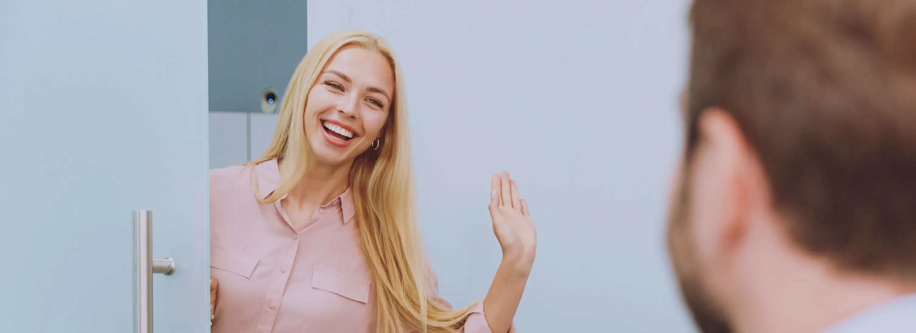 A photo of a smiling woman with long blonde hair waving at a person in the foreground.